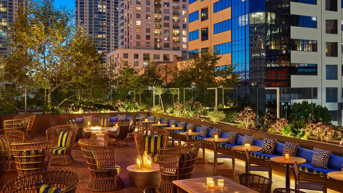 A rooftop terrace at night with low seating, fire pits and lit office towers around it