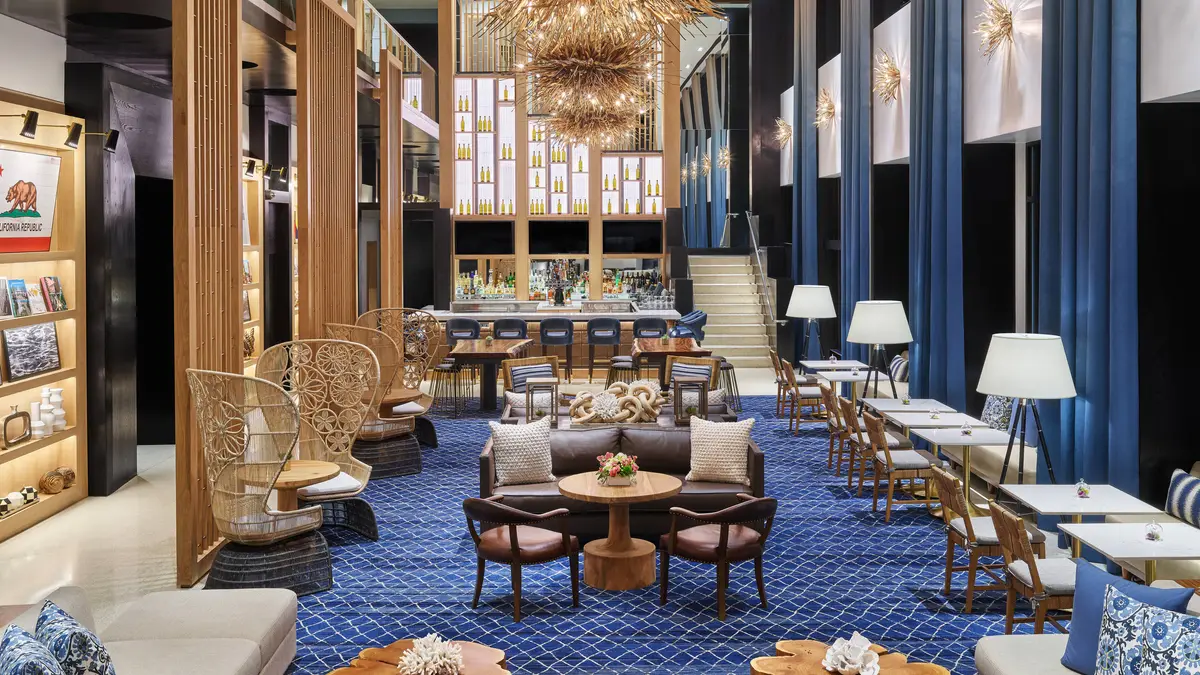 A double height lobby lounge with blue patterned carpet, tall lamps and peacock chairs