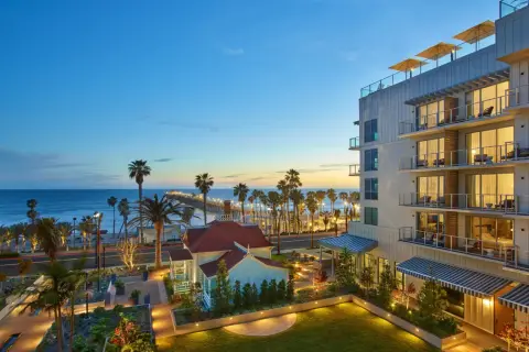 A glass and timber resort lit at dusk with lawns, palms and the beach beyond