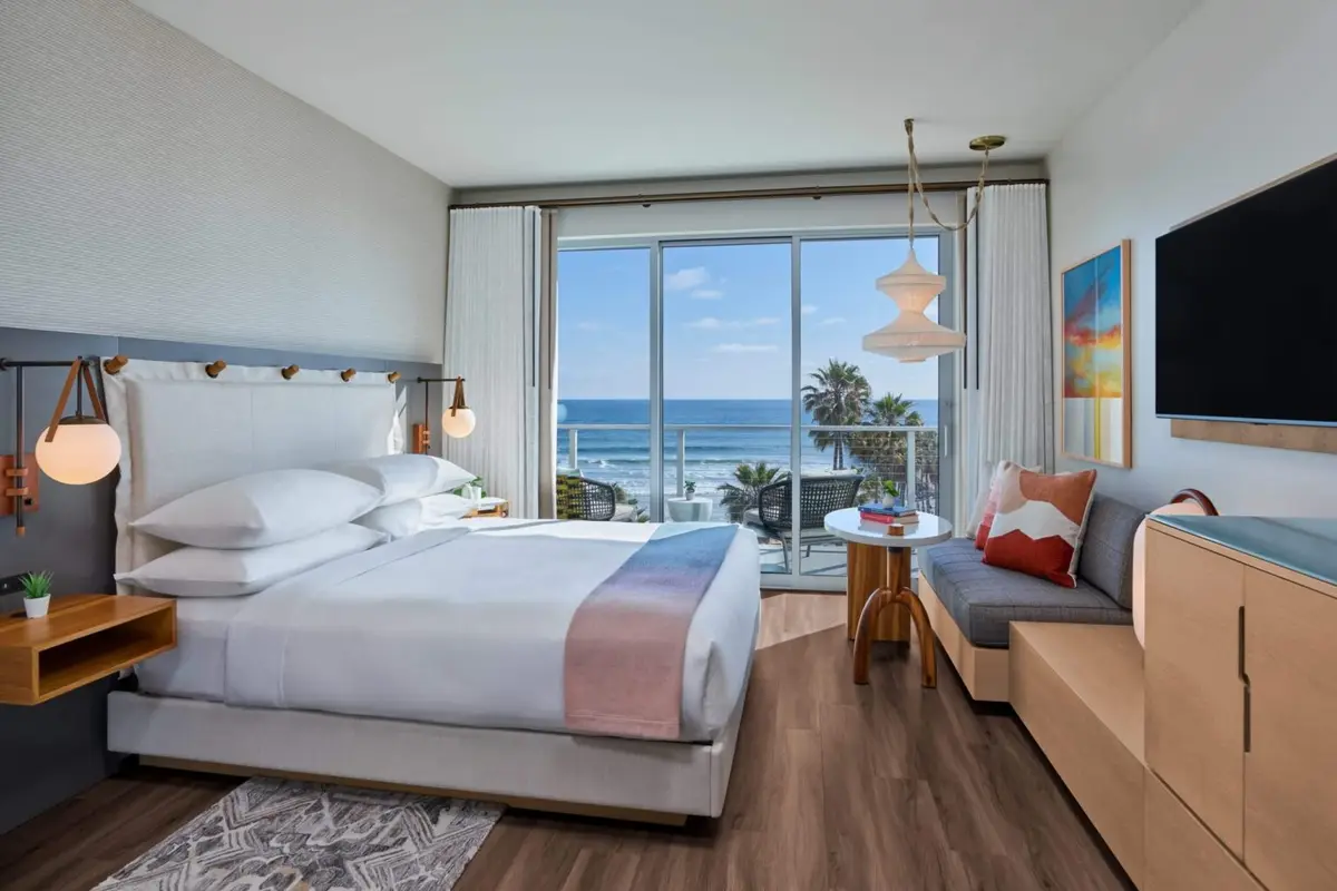 A bright guest room with a low bed, pale oak and a sliding glass wall onto the ocean