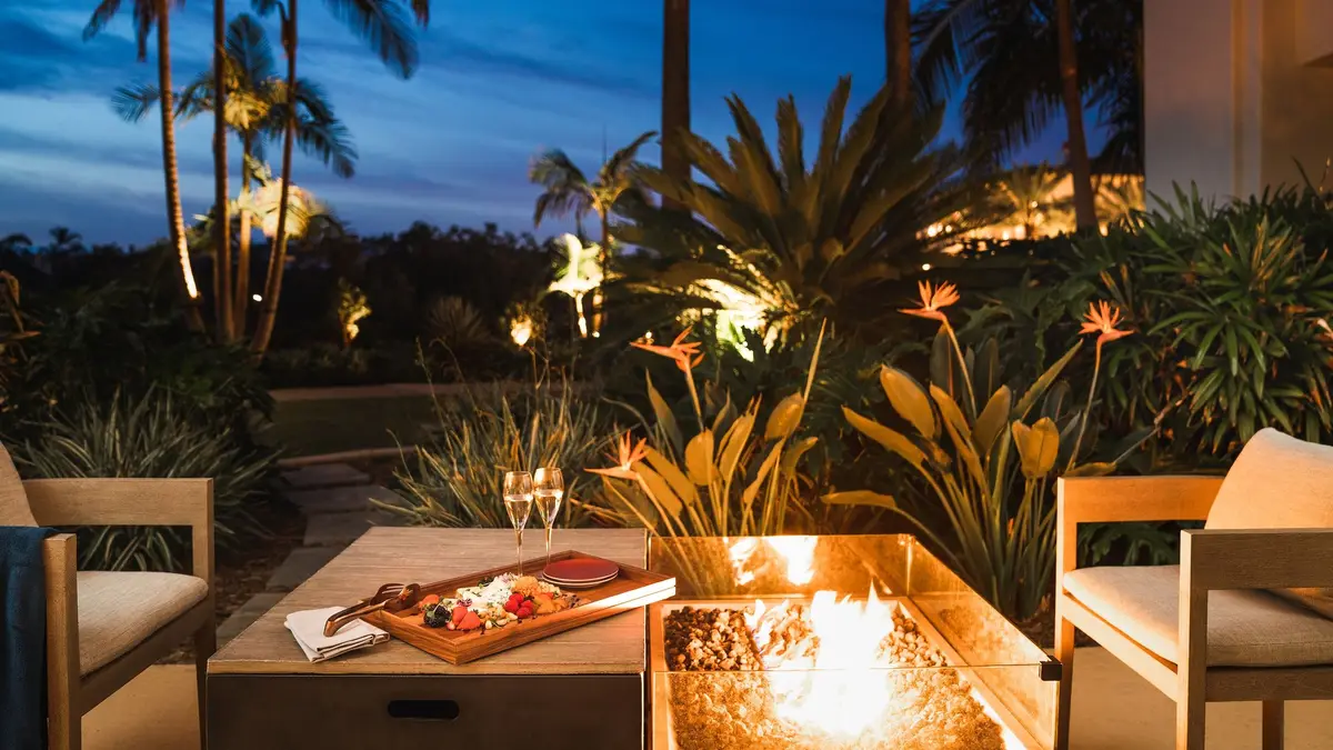 Outdoor seating around lit fire tables among palms and bird of paradise at dusk