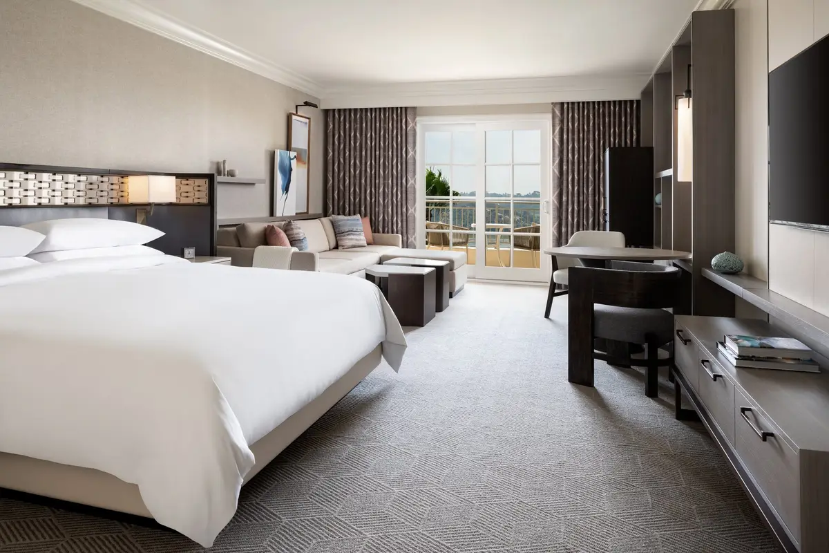 A guest room with a king bed, a long desk and French doors onto a balcony