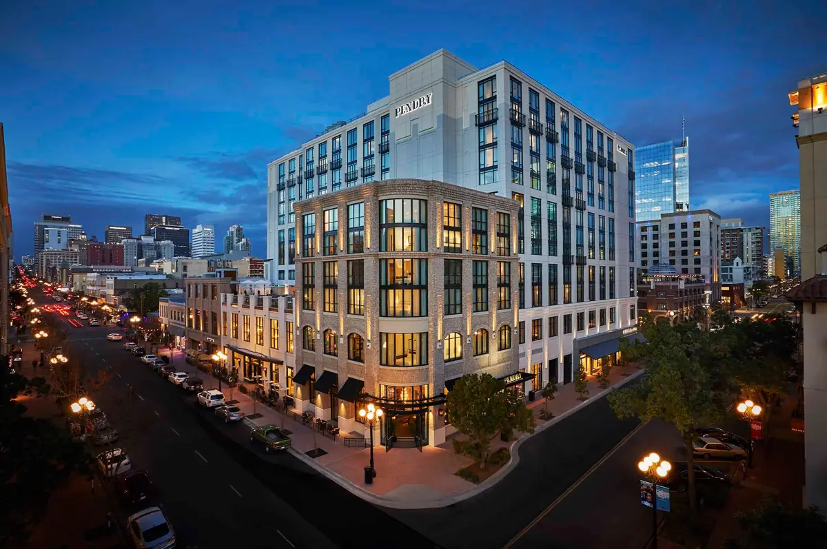 A pale stone hotel on a corner of the Gaslamp Quarter at dusk with the downtown towers behind