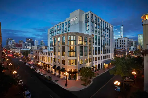 A pale stone hotel on a corner of the Gaslamp Quarter at dusk with the downtown towers behind