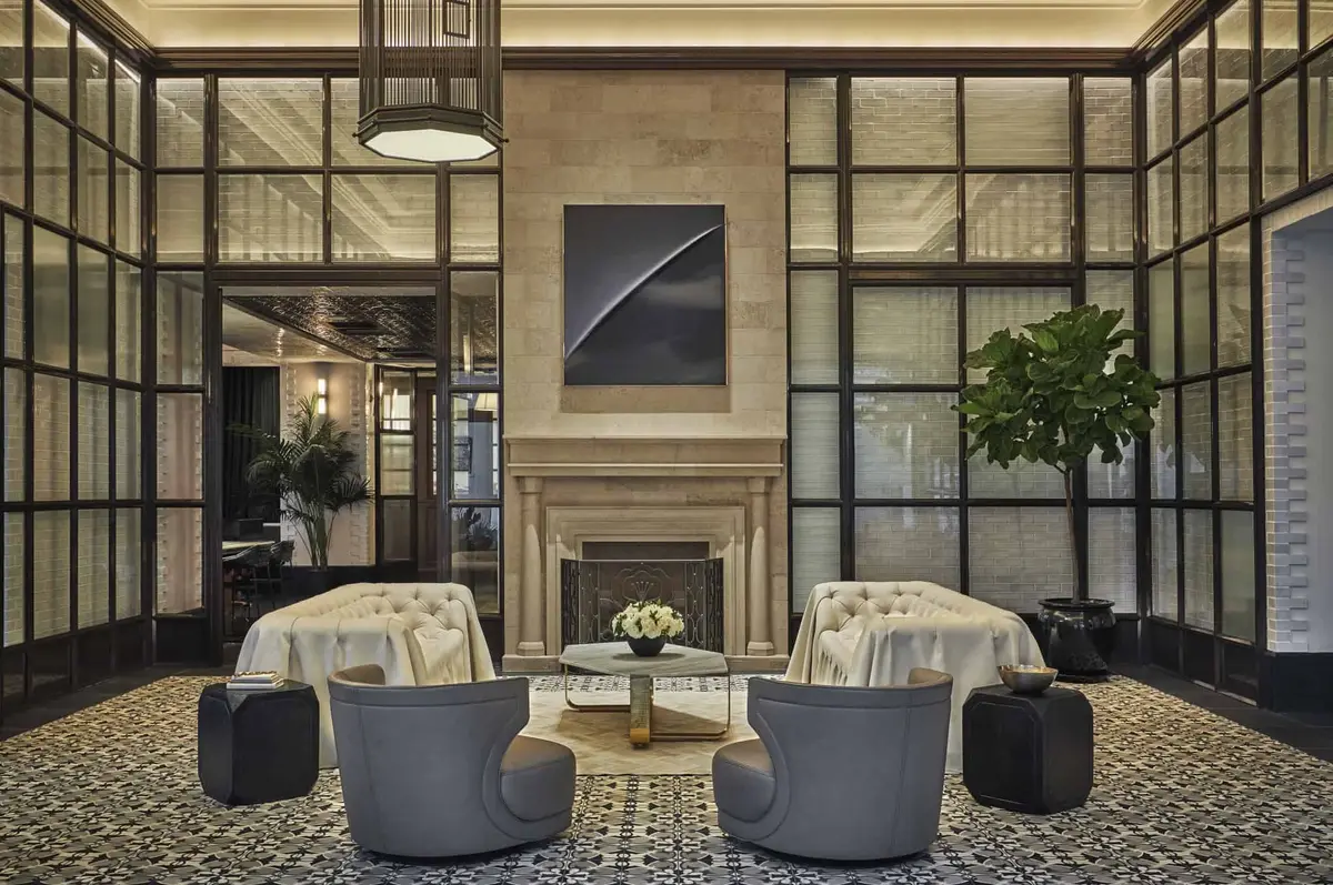 A double height lobby with a stone fireplace, tall steel framed windows and grey tub chairs