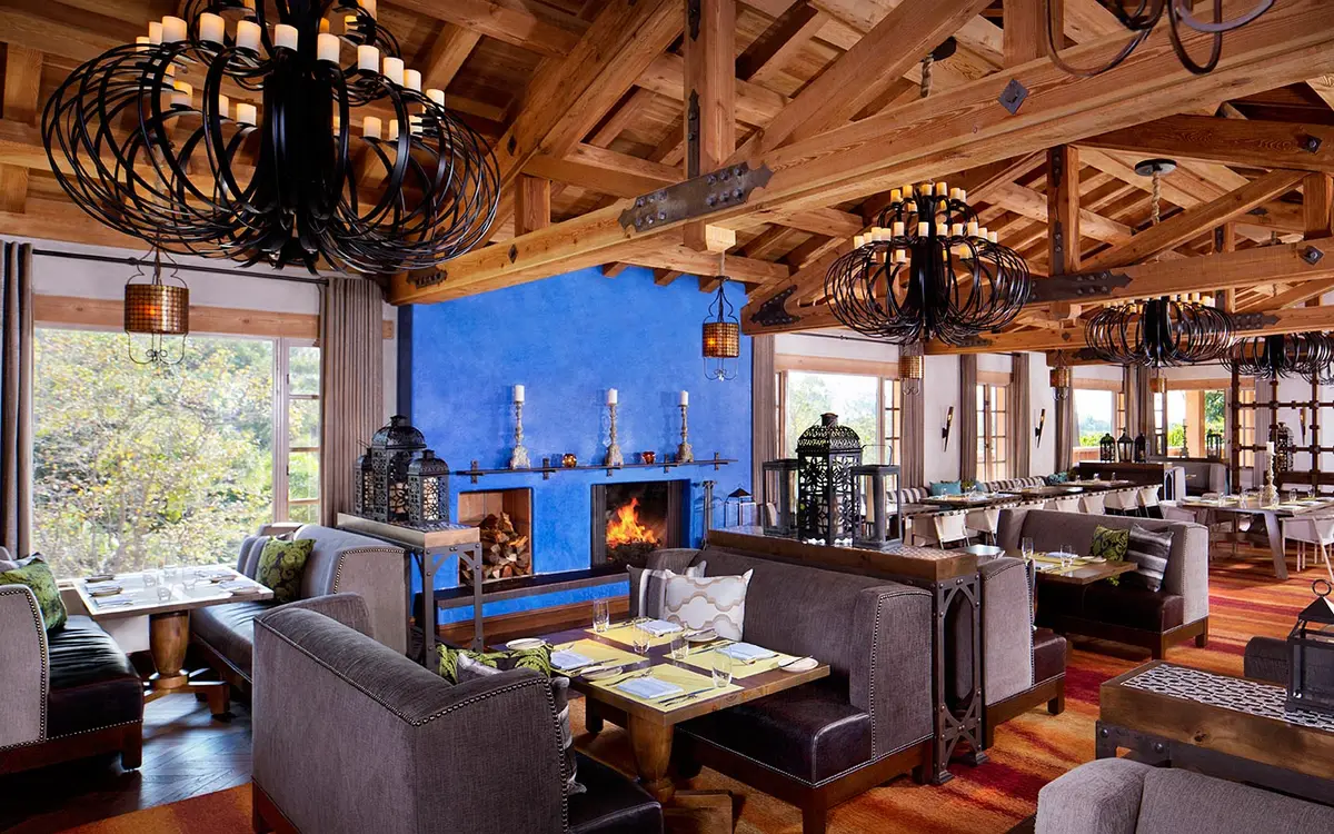 A dining room with a blue tiled fireplace, exposed beams and iron chandeliers