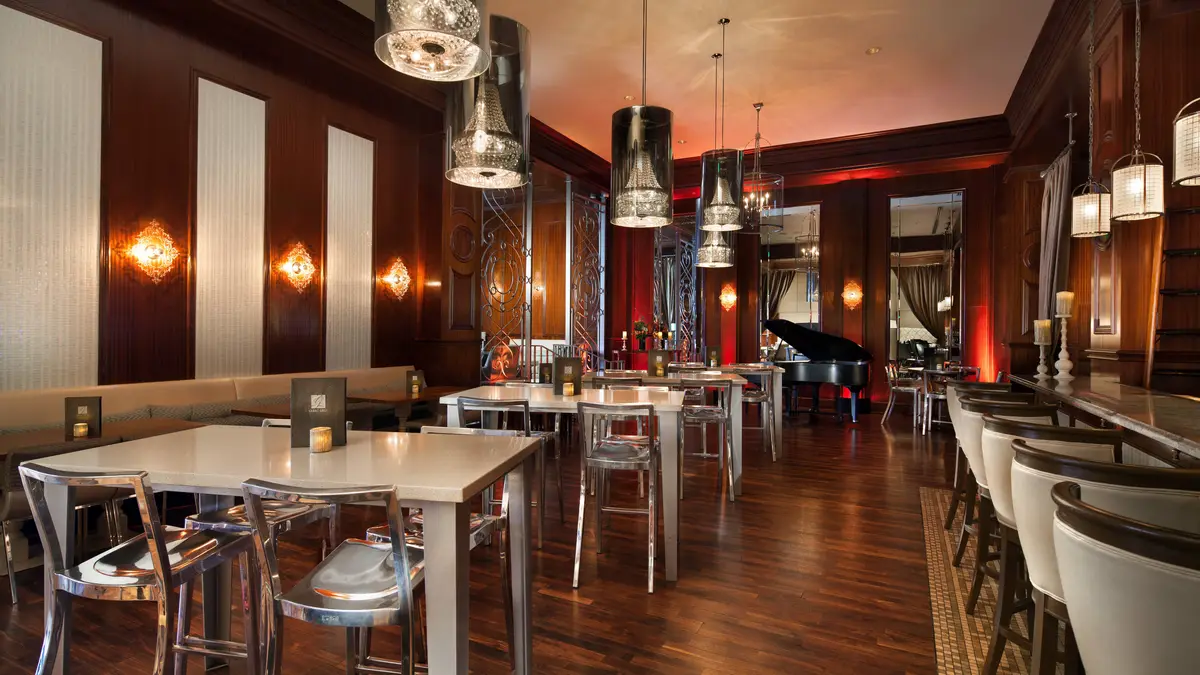 A wood panelled bar and lounge with pendant lights and a grand piano at the far end