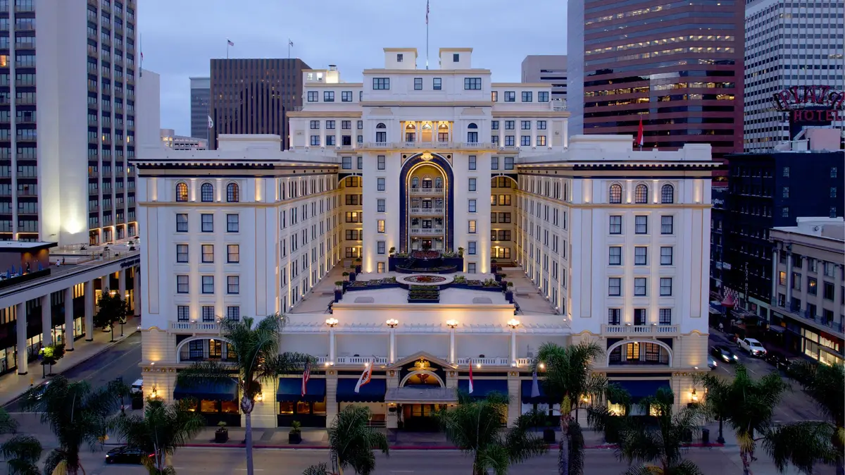 A white neoclassical hotel facade lit at twilight with downtown towers behind