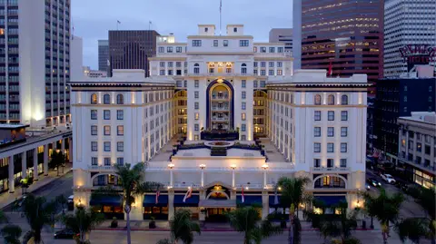 A white neoclassical hotel facade lit at twilight with downtown towers behind