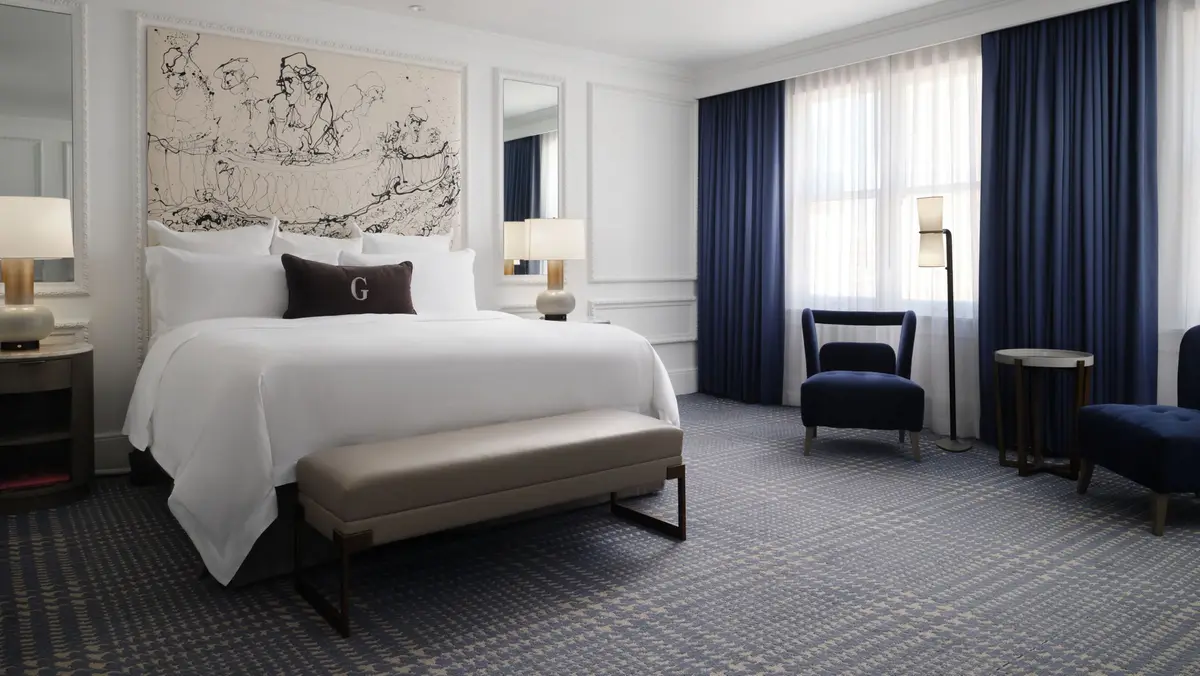 A king guest room with a white bed, navy drapes and a line drawing above the headboard
