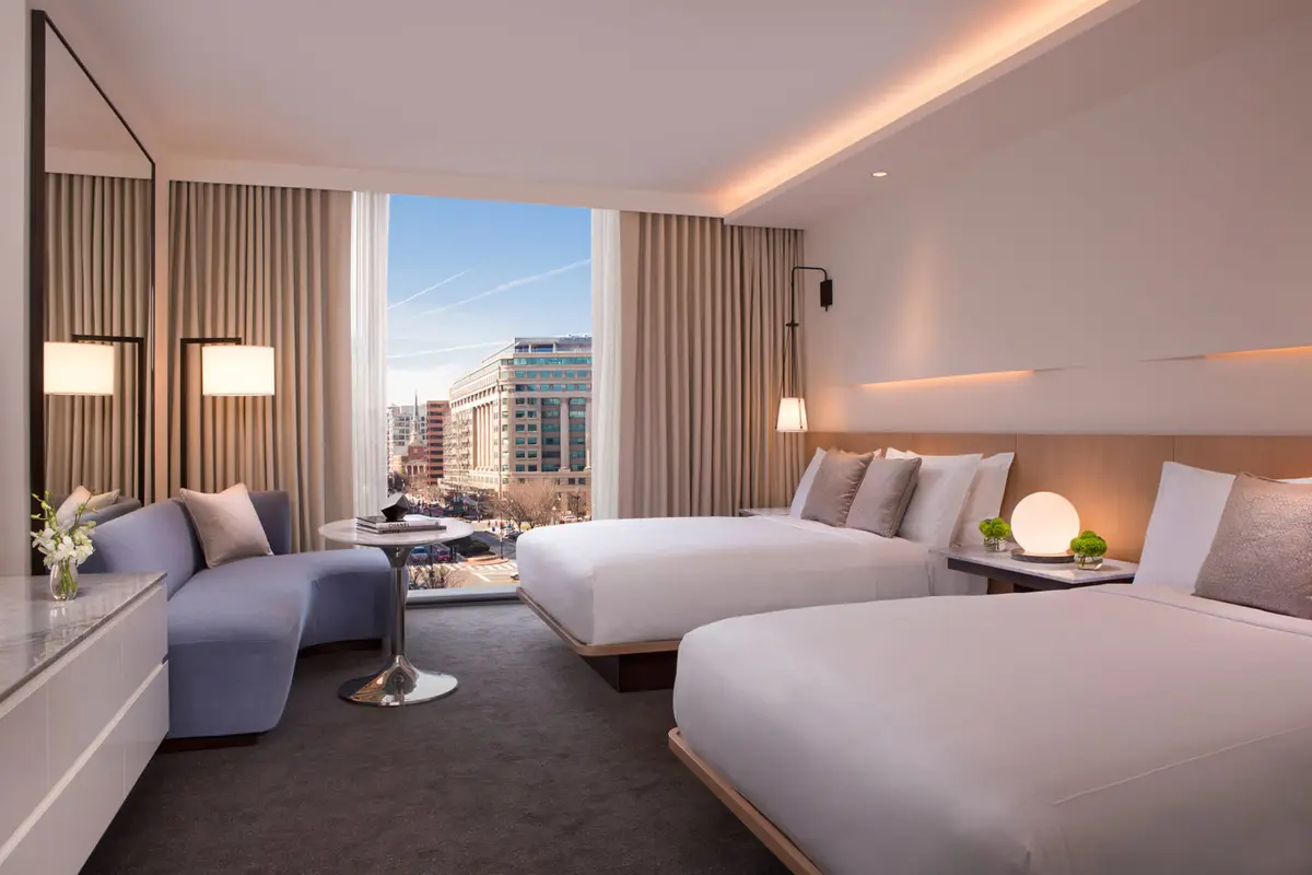 A double queen room at the Conrad Washington DC with a window seat and a city view