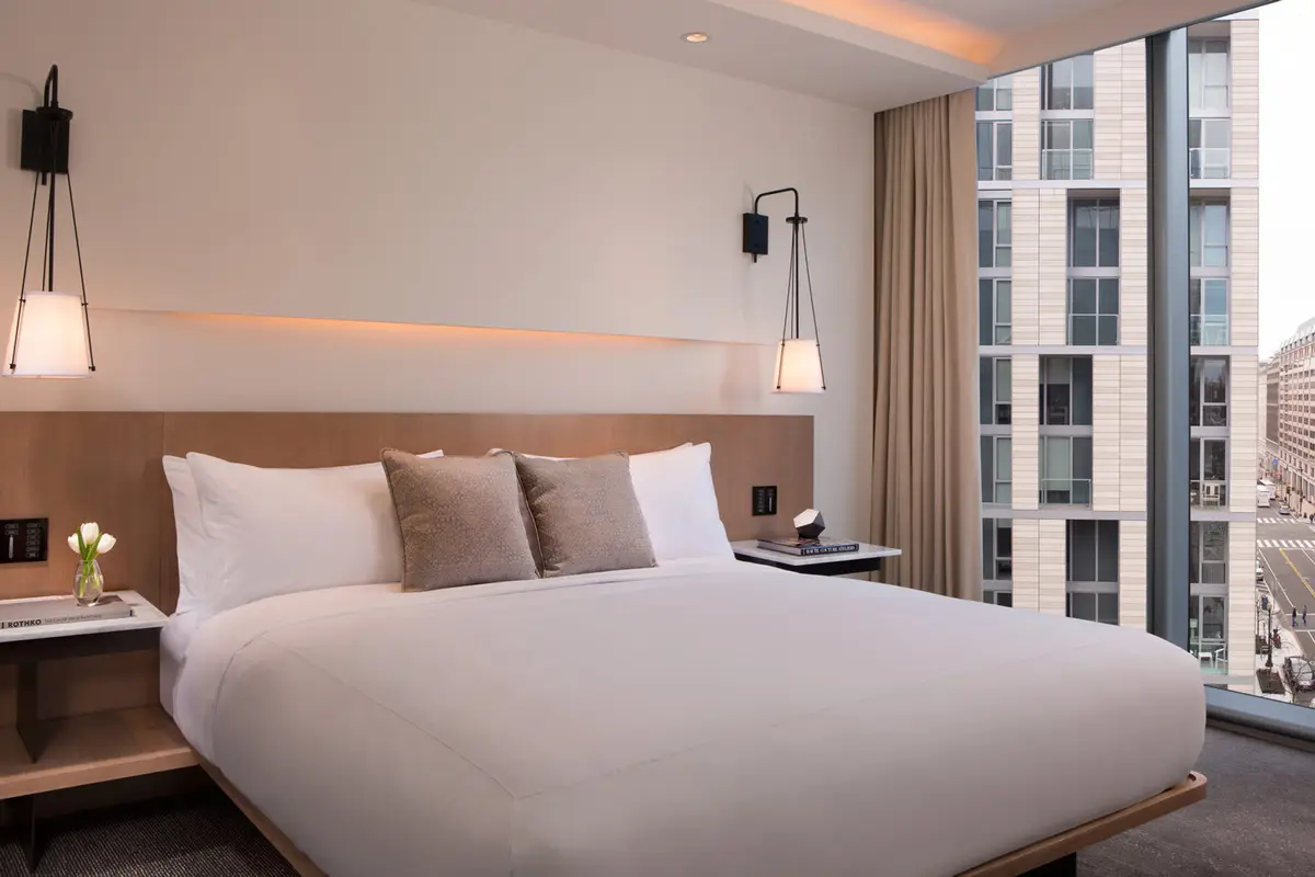 The bedroom of a park view suite at the Conrad Washington DC with pale wood and a corner window