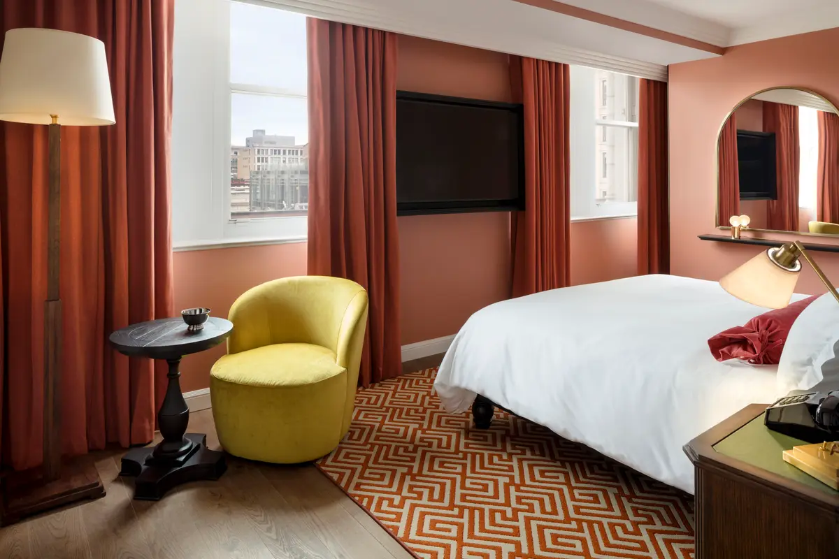 A guest room at Riggs with terracotta walls, a yellow armchair and a patterned rug
