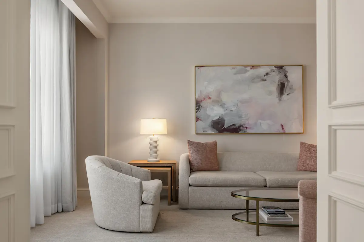 A guest room with a pale bed, two armchairs and a wide window onto the river