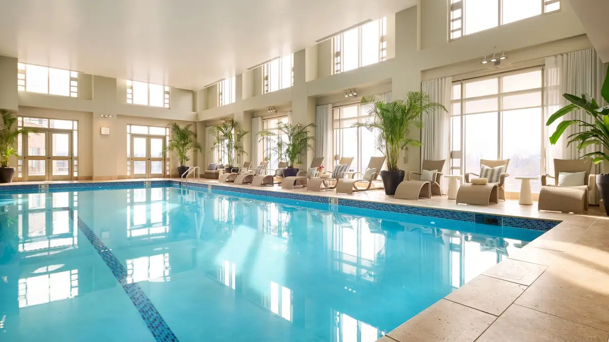 The indoor pool with tall arched windows and loungers along one side