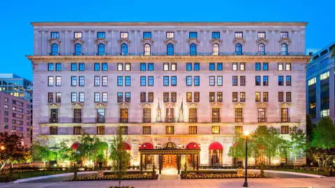 The limestone facade of the St Regis Washington DC lit at dusk with planted window boxes