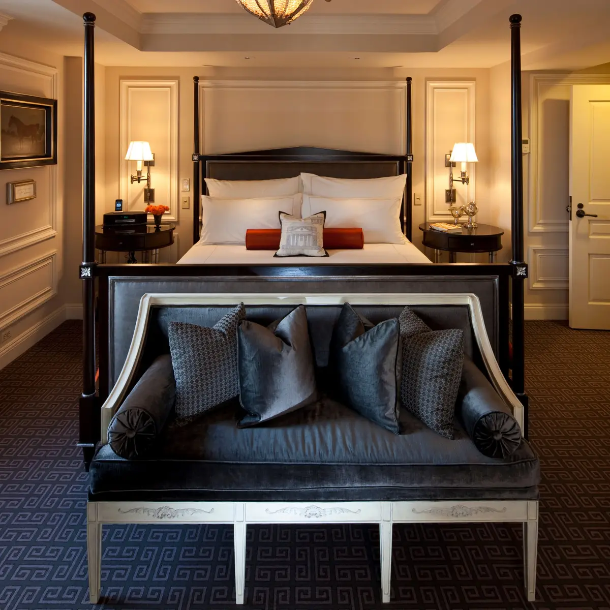 A guest bedroom at The Jefferson with a dark four poster bed and a padded bench