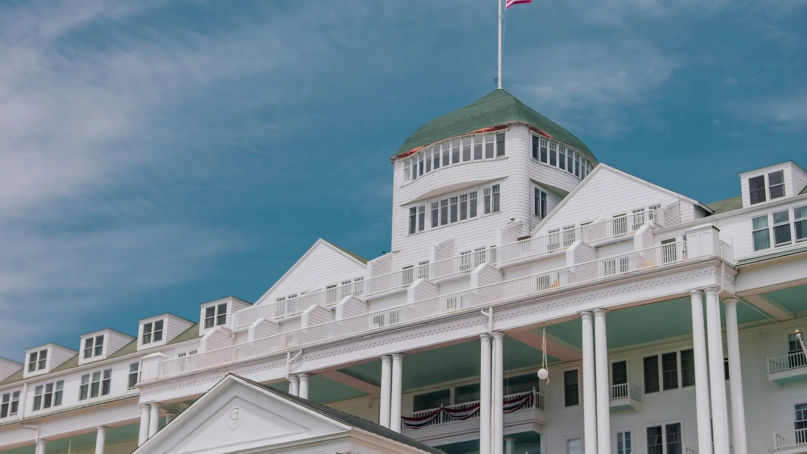 A white classical hotel facade with columned verandas standing against a clear blue sky