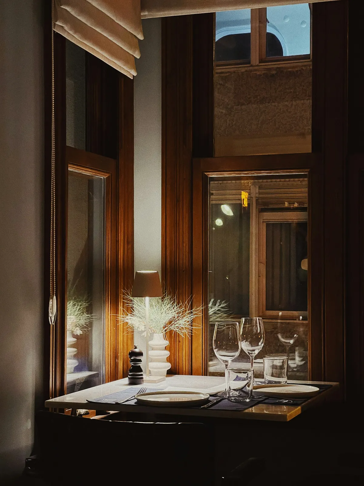 A dining table laid with white linen, polished place settings and waiting wine glasses