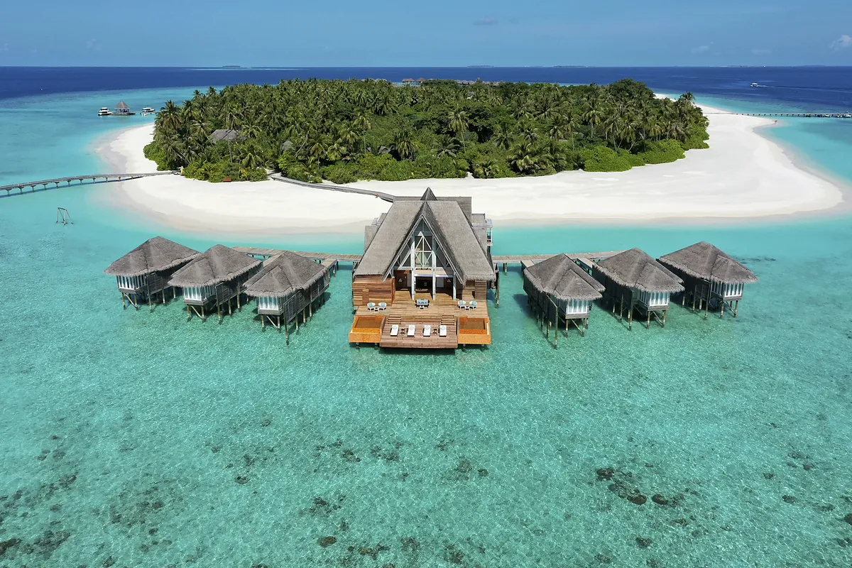 Aerial view of the spa island and overwater villas at Anantara Kihavah Maldives Villas