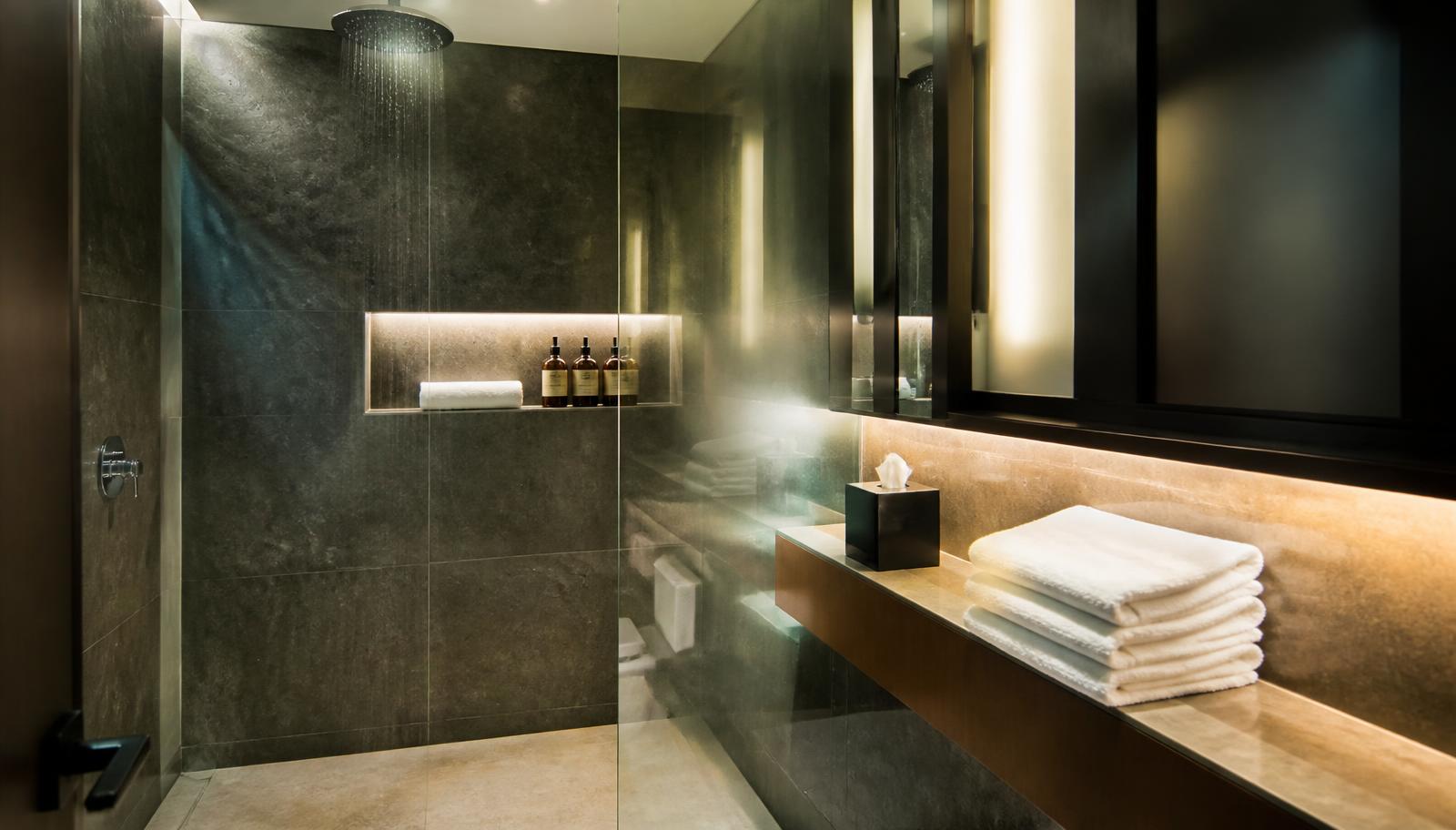 Private airport lounge shower suite with rainfall shower, slate tiling, folded white towels and warm lighting