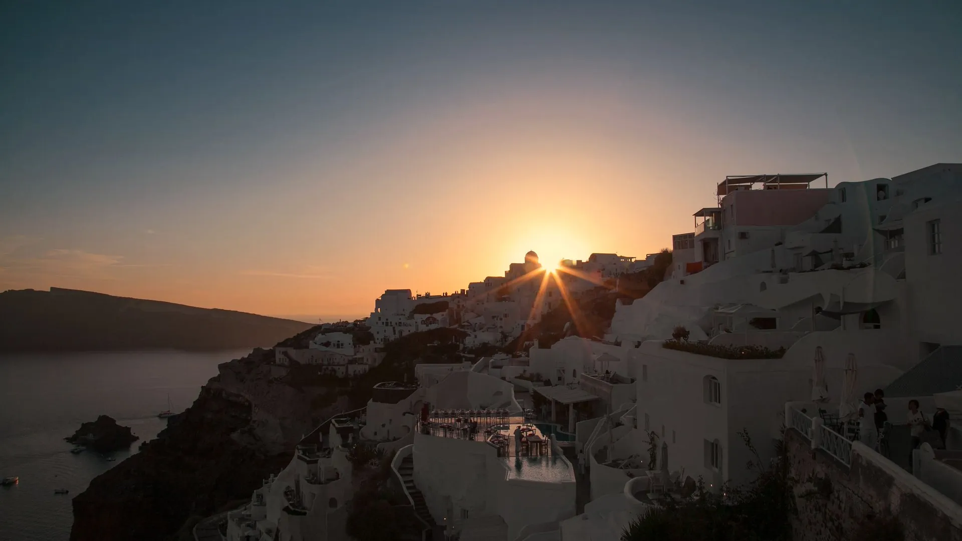 Sunset over the whitewashed clifftop village of Oia, Santorini, with the caldera below and the Aegean stretching to the horizon