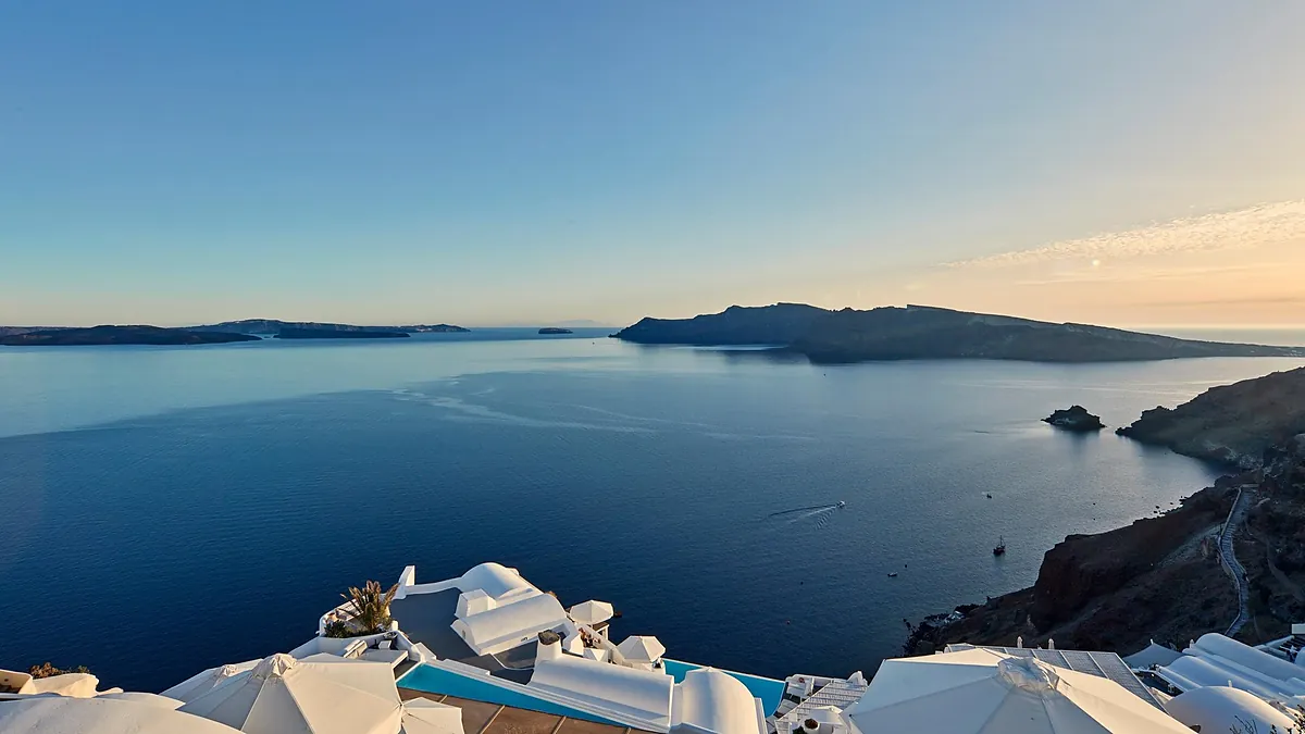One of the three infinity pools at Katikies Santorini carved into the Oia cliff, framed by white umbrellas above the caldera