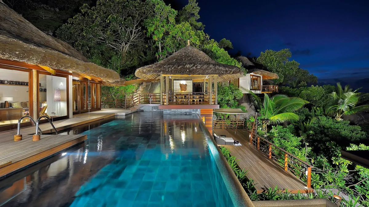 Villa pool at dusk with a thatched pavilion at Constance Lémuria, Praslin, Seychelles
