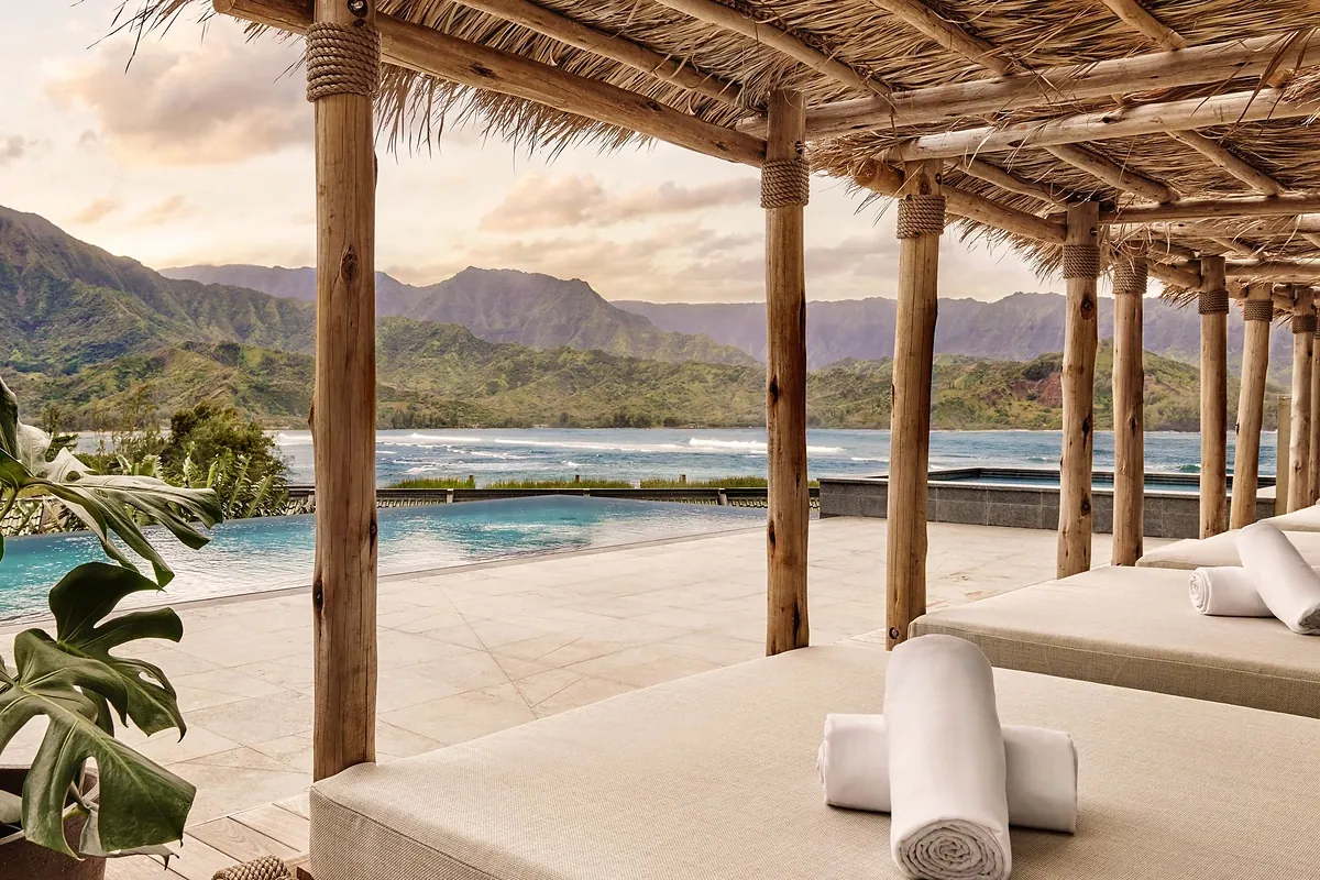 Resort pool terrace above Hanalei Bay on Kauai with green waterfall covered mountains behind